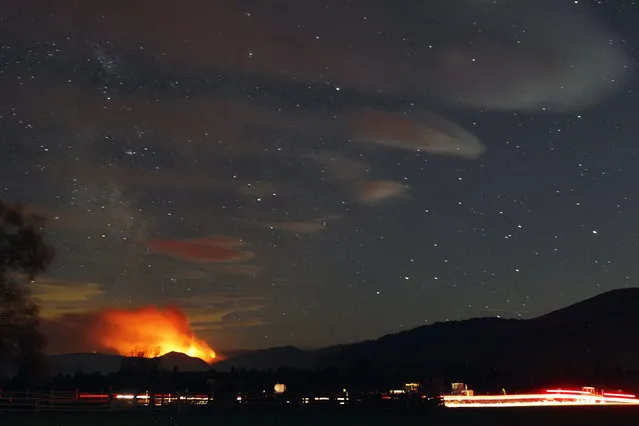 In this photo taken with a long shutter speed on Thursday night, August 20, 2015, the Black Canyon fire lights up the night sky in Chelan, Wash. Washington Gov. Jay Inslee says his state is facing an “unprecedented cataclysm” from the many fires raging across the region. (Photo by Genna Martin/The Herald via AP Photo)
