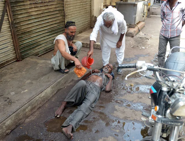 A Pakistani resident helps a heatstroke victim at a market area during a heatwave in Karachi on June 23, 2015. The death toll from a heatwave in southern Pakistan on June 23 passed 450 as medics battled to treat victims after imposing a state of emergency in hospitals, health officials said. (Photo by Rizwan Tabassum/AFP Photo)