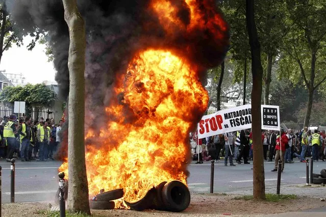 French non-union self-employed workers set fire to tyres stand near burning tyres during a protest against the RSI (social security for independent workers) near the Hotel Matignon, offices of French Prime minister in Paris, France, September 21, 2015. The banner reads “Stop tax increases”. (Photo by Charles Platiau/Reuters)
