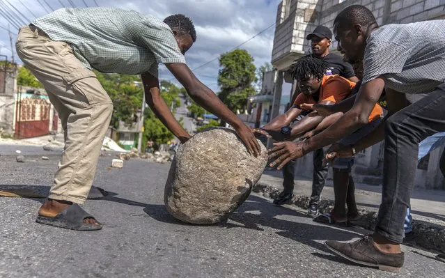 People work together to move a rock in order to set up a barricade in protest over the death of journalist Romelo Vilsaint, in Port-au-Prince, Haiti, Sunday, October 30, 2022. (Photo by Ramon Espinosa/AP Photo)
