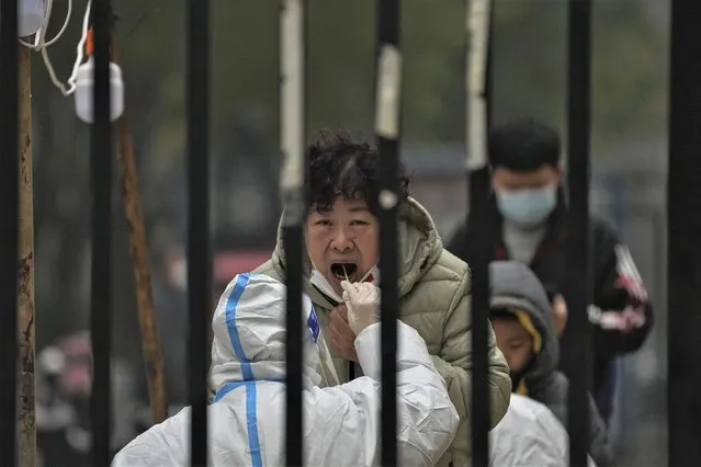 A woman has her routine COVID-19 test at a coronavirus testing site setup inside a residential compound in Beijing, Thursday, November 24, 2022. China is expanding lockdowns, including in a central city where factory workers clashed this week with police, as its number of COVID-19 cases hit a daily record. (Photo by Andy Wong/AP Photo)