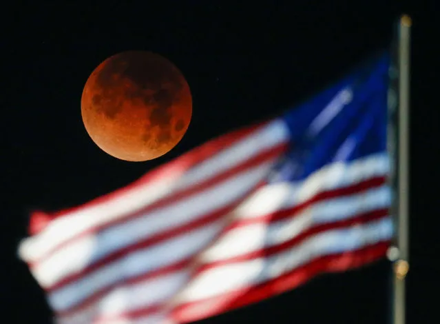 A rare occurrence called a “Super Blue Blood Moon” is seen behind the U.S. flag at Santa Monica Beach in Santa Monica, Calif., Wednesday, January 31, 2018. (Photo by Ringo H.W. Chiu/AP Photo)