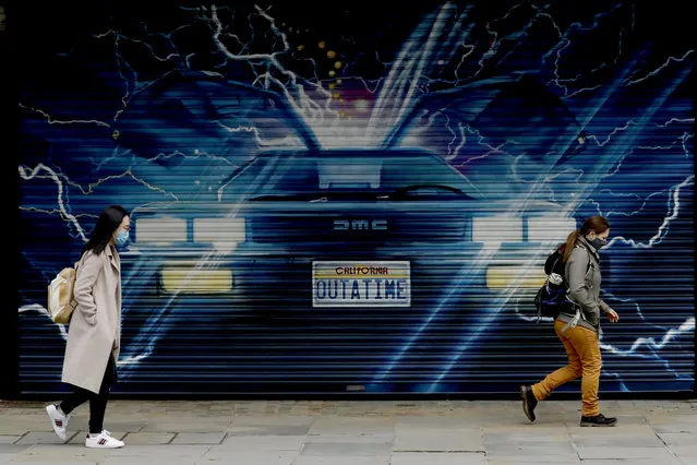 People wearing face masks to try to curb the spread of coronavirus walk past an image for “Back to the Future the Musical” on a shutter outside the Adelphi Theatre in London, Thursday, October 15, 2020. London Mayor Sadiq Khan says he expects the government will move the UK capital to a higher level of COVID-19 restrictions later Thursday. The move comes as infection rates in the capital are rising.  Khan says the city will soon reach an average of 100 cases per 100,000, a level some boroughs have already surpassed. (Photo by Matt Dunham/AP Photo)