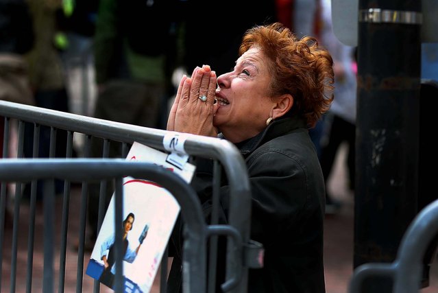 A distraught woman kneels and prays near the finish line. (Photo by John Tlumacki/The Boston Globe)