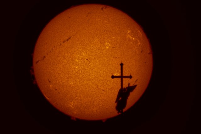 In this photo, taken by a solar telescope, the city landmark, a weather vane in the form of an angel fixed atop a spire of the Saints Peter and Paul Cathedral, is silhouetted against the sun that shows a few solar activity zones, in St. Petersburg, Russia, Thursday, August 21, 2025. (Photo by Dmitri Lovetsky/AP Photo)