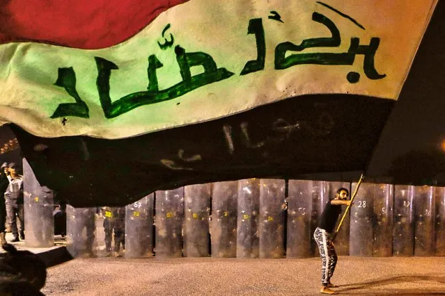 A protester waves an Iraqi flag while Security forces surround the protest site during ongoing anti-government protests in Basra, Iraq, Wednesday, November 4, 2020. (Photo by Nabil al-Jurani/AP Photo)