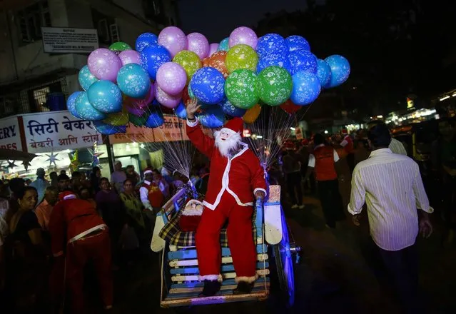 A man dressed in a Santa Claus outfit waves at the crowd as he rides with balloons on a horse cart during Christmas celebrations in Mumbai December 23, 2014. (Photo by Danish Siddiqui/Reuters)