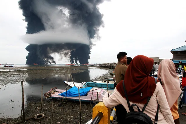 People watch the rising black smoke from a burned oil spill at the waters in Balikpapan, Indonesia on March 31, 2018. A cargo ship caught fire in waters off East Kalimantan province in central Indonesia on Saturday, leaving two people dead and two others missing, an official said. (Photo by Xinhua News Agency/Rex Features/Shutterstock)
