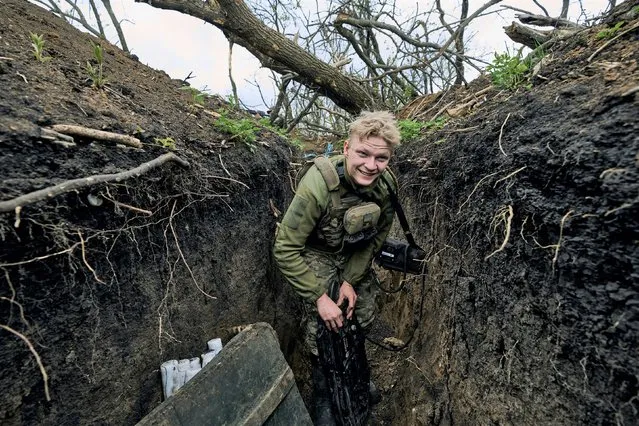 A Ukrainian soldier smiles as he stands in a trench on the frontline near Avdiivka, an eastern city where fierce battles against Russian forces have been taking place, in the Donetsk region, Ukraine, Friday, April 28, 2023. (Photo by Libkos/AP Photo)