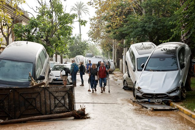 Residents walk past damaged vehicles lining a flooded street in Picana, in the province of Valencia, eastern Spain, 30 October 2024. The intense rainfall impacting the eastern part of the country resulted in at least 62 lives being lost in the province of Valencia due to the flooding. The State Meteorological Agency (AEMET) has issued red alerts for rainfall in multiple regions of the province of Valencia, caused by the severe storm DANA. (Photo by Biel Aliño/EPA/EFE)