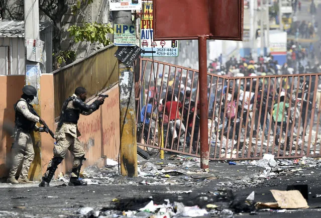 A member of the Haitian police points his gun at people to avoid looting in shops in Delmas, a commune near Port au Prince during protests against the rising price of fuel, on July 8, 2018. Fresh looting broke out on the streets of Haiti's capital on July 8, 2018, despite calls for calm after two days of deadly protests over ultimately suspended fuel price hikes. In the heart of Port-au-Prince, AFP journalists saw some shops ransacked while groups began erecting new road barricades on the capital's outskirts. (Photo by Hector Retamal/AFP Photo)