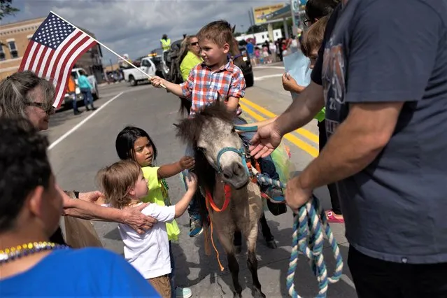 Levi Gale, 5, waves a U.S. flag as children approach to pet his miniature horse Lady Bug during the Fourth of July Independence Day parade in Texas City, Texas, U.S., July 4, 2023. (Photo by Adrees Latif/Reuters)