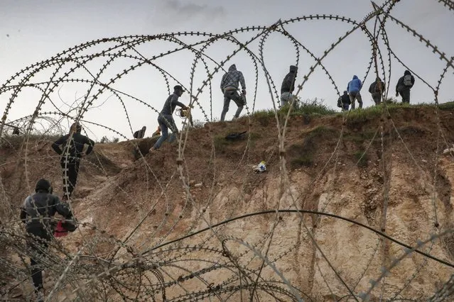 Palestinians go through a barbed-wire fence into Israel as they attempt to cross to reach their workplaces close to the Israeli checkpoint of Mitar, near Hebron in the occupied West Bank on March 1, 2021, despite a nationwide lockdown enforced by the Israeli authorities to stem a surge in COVID-19 coronavirus cases. (Photo by Hazem Bader/AFP Photo)