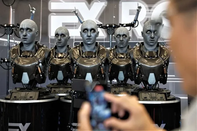 A visitor uses a phone in front of humanoid robots developed by EXRobots at the Beijing World Robot Conference (WRC) 2023 in Beijing, China on August 17, 2023. (Photo by Tingshu Wang/Reuters)