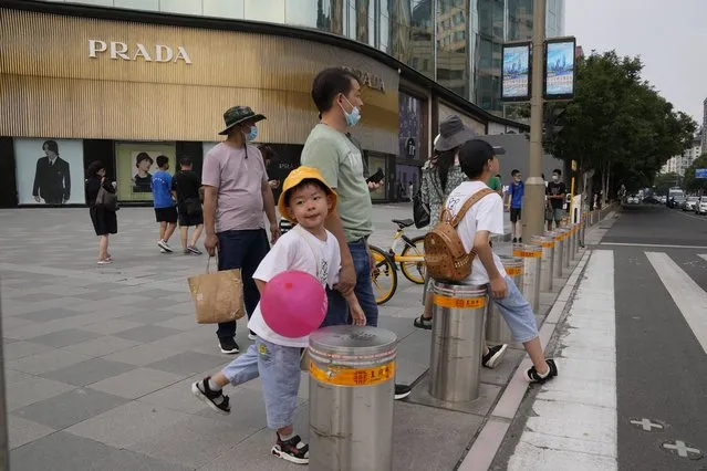 A child waits to cross a road near high end shops at the Wangfujing retail street in Beijing Wednesday, July 14, 2021. (Photo by Ng Han Guan/AP Photo)