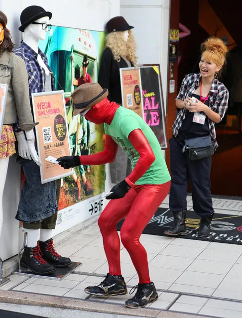 A dude(?) in a red bodysuit(?) trys to do drum up business(?) by handing coupon cards(?) to a mannequin(?) in front of a store on Harajuku's famous Takeshita Dori fashion street. Tokyo, Japan. (Photo by Aaron Webb)
