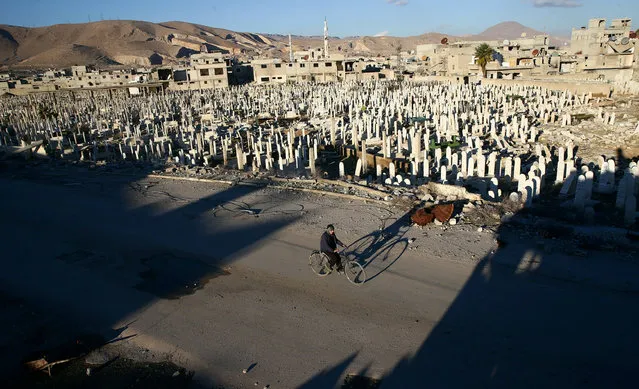 A civilian rides a bicycle past a cemetery in the rebel held besieged Douma neighbourhood of Damascus, Syria January 3, 2017. (Photo by Bassam Khabieh/Reuters)