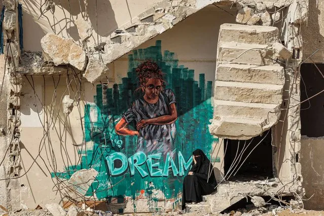 A woman sits along the broken steps of a partially-collapsed building destroyed by bombardment during the May 2021 confliict between Hamas and Israel, next to a graffiti mural depicting a girl with an English caption below reading “I've dream”, in Gaza City on August 12, 2021. (Photo by Mohammed Abed/AFP Photo)