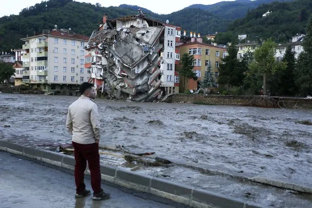 A man looks on as flood waters sweep by in Bozkurt town of Kastamonu province of Turkey, Thursday, August 12, 2021. The floods triggered by torrential rains battered the Black Sea coastal provinces of Bartin, Kastamonu, Sinop and Samsun on Wednesday, demolishing homes and bridges and sweeping cars away by torrents. Helicopters scrambled to rescue people stranded on rooftops. (Photo by IHA via AP Photo)
