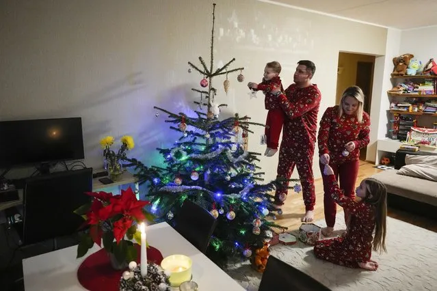 Sergei Sidorovich, left, and Marina Begunkova decorate a Christmas tree with their children Anna, right, and Misha, left, in their apartments in Tallinn, Estonia, Thursday, December 21, 2023. In Estonia, as in many parts of the world, trees covered with lights brighten up homes and town squares during the Winter Solstice and Christmas festivities afterwards. (Photo by Pavel Golovkin/AP Photo)