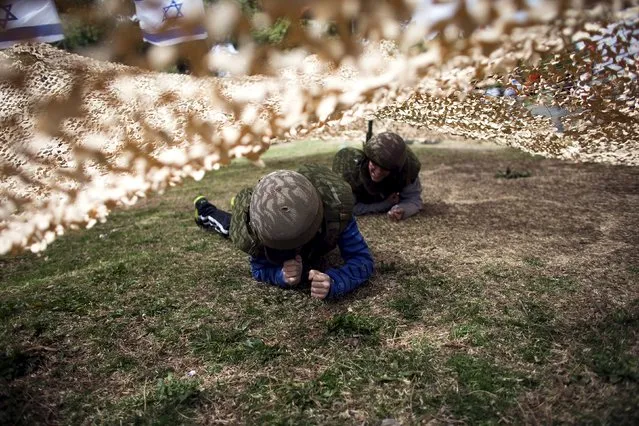 Israeli boys play under a camouflage net during a display of Israeli Defense Forces (IDF) equipment and abilities at the West Bank settlement of Kiryat Arba, April 23, 2015, during celebrations for Israel's Independence Day, marking the 67th anniversary of the creation of the state. (Photo by Ronen Zvulun/Reuters)
