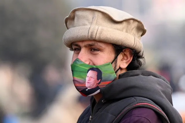 A supporter of jailed farmer prime minister Imran Khan wearing facemask displaying his picture stands along a street in Rawalpindi on January 24, 2024, ahead of Pakistan's upcoming general election. (Photo by Farooq Naeem/AFP Photo)
