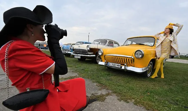 A woman poses by a retro car, an exhibit of OldCarLand festival, at the open-air State Aviation Museum in Kiev during the festival's opening on September 17, 2021. (Photo by Sergei Supinsky/AFP Photo)