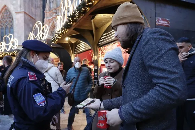 A police officer checks the vaccination status of visitors during a patrol on a Christmas market in Vienna, Austria, Friday, November 19, 2021. Austrian Chancellor Alexander Schallenberg says the country will go into a national lockdown to contain a fourth wave of coronavirus cases. Schallenberg said the lockdown will start Monday, Nov.22 , and initially last for 10 days. (Photo by Lisa Leutner/AP Photo)