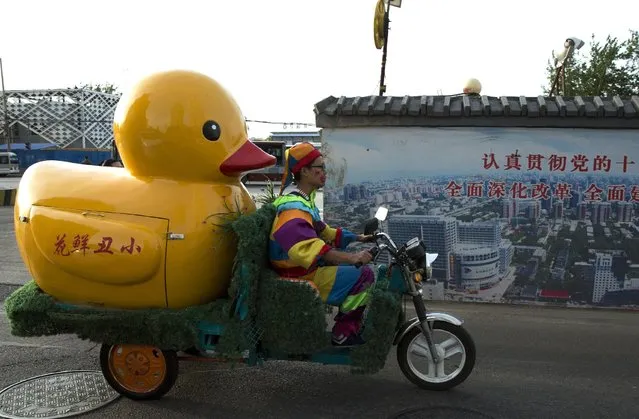 A delivery man for a florist dressed as a clown makes his rounds past government slogans calling for deepening reforms in Beijing Tuesday, May 5, 2015. Government propaganda is a common sight in the Chinese capital, a reminder it is also the political center of China. (Photo by Ng Han Guan/AP Photo)