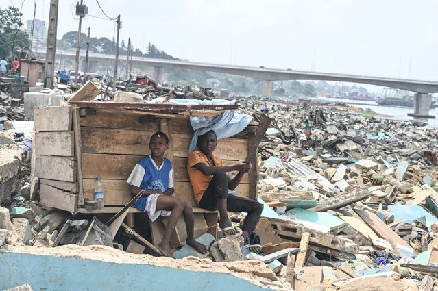 Resdidents sit near a structure amid rubbles of demolished houses in Boribana, district of Attecoube in Abidjan on Febuary 25, 2024. The governor of the district of Abidjan begun an operation to demolish high-risk neighborhoods in Abidjan. (Photo by Issouf Sanogo/AFP Photo)