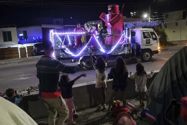 Venezuelan migrants try to catch candy thrown from a Christmas truck as they stand outside their tents, where they live in Iquique streets, Chile, Saturday, December 11, 2021. (Photo by Matias Delacroix/AP Photo)
