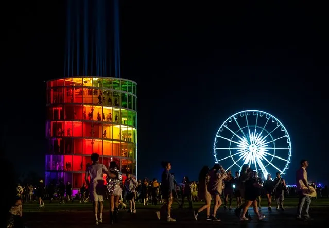 Festivalgoers walk between venues with "Spectra" by NEWSUBSTANCE and the iconic Ferris wheel seen in the background during the Coachella Valley Music and Arts Festival in Indio, Calif., on Friday, April 12, 2024. (Photo by Andy Abeyta/The Desert Sun)