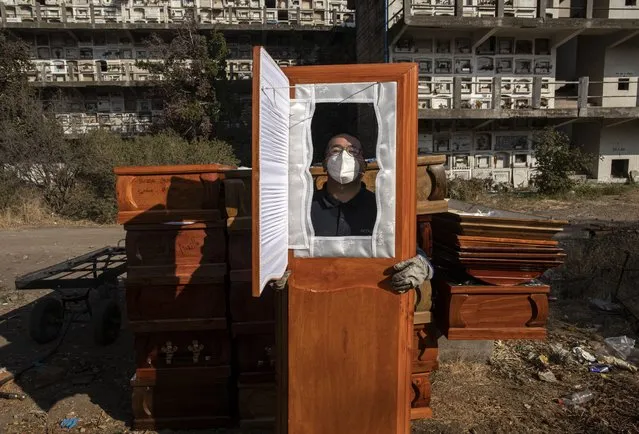 A funeral worker asks for his photo to be taken through one of the used coffins he is moving following cremations at La Recoleta cemetery during the coronavirus pandemic in Santiago, Chile, Monday, April 19, 2021. (Photo by Esteban Felix/AP Photo)