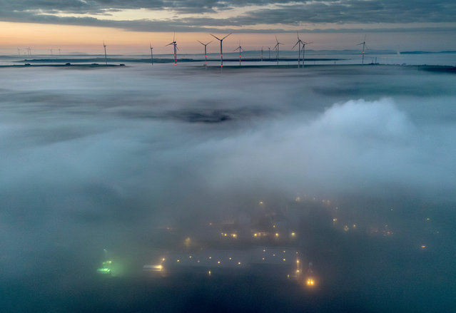 Fog floats over a wind energy plant near Stetten, some 20 kilometres north of Kaiserslautern, Germany, as the sun rises on Tuesday, March 19, 2024. (Photo by Michael Probst/AP Photo)