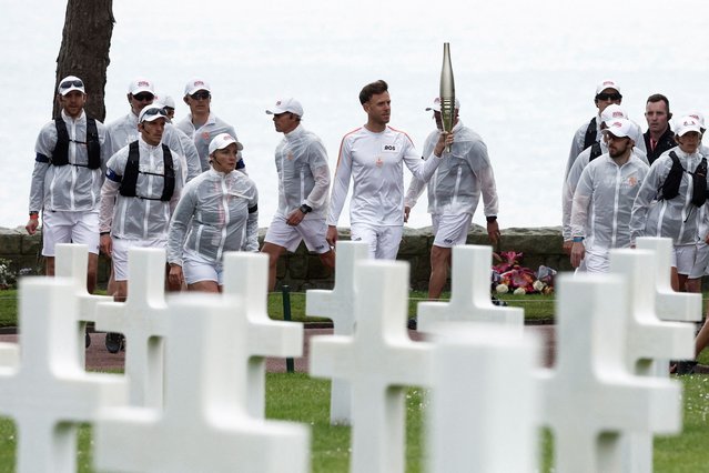 Torchbearer Nicolas-Marie Daru holds the Olympics torch during the relay ahead of the Paris 2024 Olympic games, at the World War II Normandy American Cemetery and Memorial, in Colleville-sur-Mer, situated above Omaha Beach, Normandy region, France on May 30, 2024. (Photo by Benoit Tessier/Reuters)