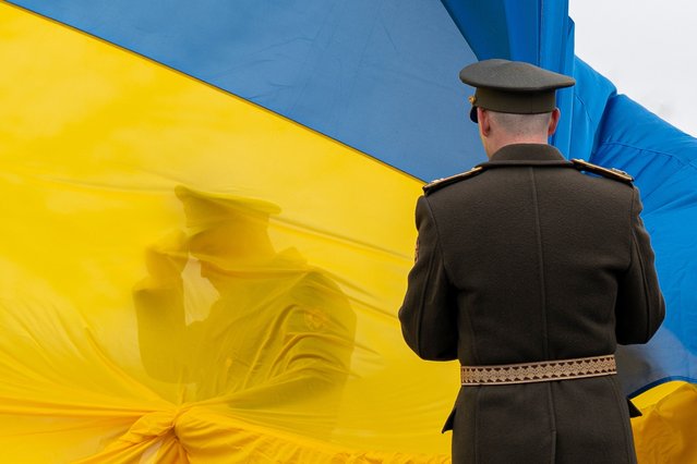 Ukrainian military personnel hold a Ukrainian national flag during an event to mark the anniversary of the city.s de-occupation in Bucha, Ukraine, on Friday, March 31, 2023. The prime ministers of Slovakia, Slovenia and Croatia visited to mark the one-year liberation of the town of Bucha, near the capital, from a brutal, weeks-long Russian occupation. (Photo by Andrew Kravchenko/Bloomberg)