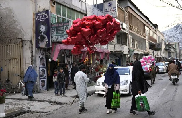 Afghan women pass next of a street vendor who sells red heart-shaped balloons during the Valentine's Day, in Kabul, Afghanistan, Monday, February 14, 2022. (Photo by Hussein Malla/AP Photo)