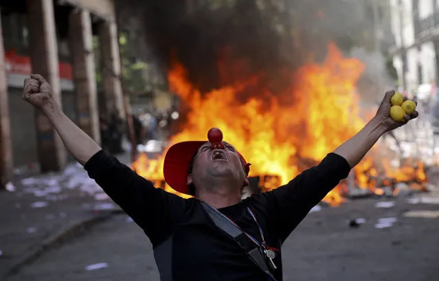 An anti-government demonstrator screams in font of a burning barricade in Santiago, Chile, Tuesday, October 22, 2019. Protests in the country have spilled over into a fifth day, even after President Sebastian Pinera cancelled the subway fare hike that prompted rioting, arson and violent clashes that have almost paralyzed the country. (Photo by Rodrigo Abd/AP Photo)