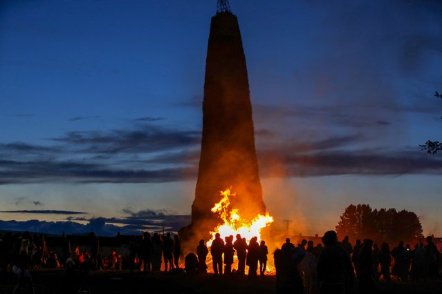 People gather to watch the 11th night bonfire prior to being burnt on the Craigyhill estate in Larne, Northern Ireland on July 11, 2024. The bonfire that builders claim is the tallest in the world, is set alight in protestant areas of Northern Ireland on the eve of the 12th July, to mark the start of Orange celebrations celebrating the defeat of the Catholic King James, by William of Orange in the battle of the Boyne in 1690. (Photo by Paul Faith/AFP Photo)