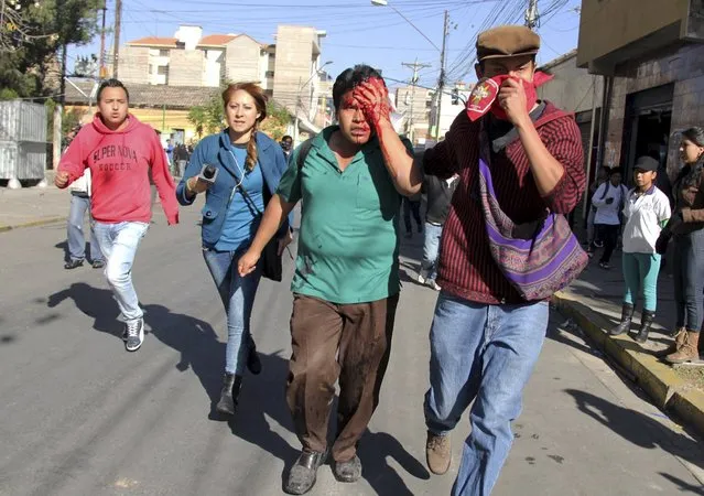 An injured student runs with classmates after being hit in the head by a tear gas canister during clashes with riot policemen in Cochabamba, southeast of La Paz, July 30, 2015. Students from San Simon University in Cochabamba were demanding for better academic conditions, according to local media. (Photo by Danilo Balderrama/Reuters)
