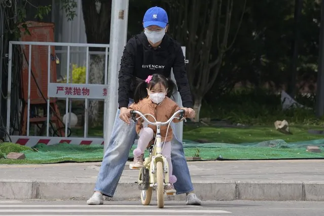 A woman and child wearing masks cross a road on Monday, May 9, 2022, in Beijing. (Photo by Ng Han Guan/AP Photo)