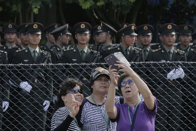 Visitors pose for a photograph in front of the Chinese soldiers as Chinese President Xi Jinping inspects the troops of People's Liberation Army (PLA) Hong Kong Garrison at the Shek Kong Barracks in Hong Kong, Friday, June 30, 2017. Xi inspected troops based in Hong Kong on Friday as he asserts Chinese authority over the former British colony China took control of 20 years ago. (Photo by Kin Cheung/AP Photo)
