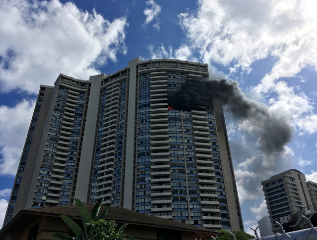 Smoke billows from a high-rise apartment building in Honolulu, Friday, July 14, 2017. Dozens of firefighters are battling the multiple-alarm fire at Marco Polo apartments that Honolulu Fire Department spokesman Capt. David Jenkins said started on the 26th floor and has spread to other units. (Photo by Audrey McAvoy/AP Photo)
