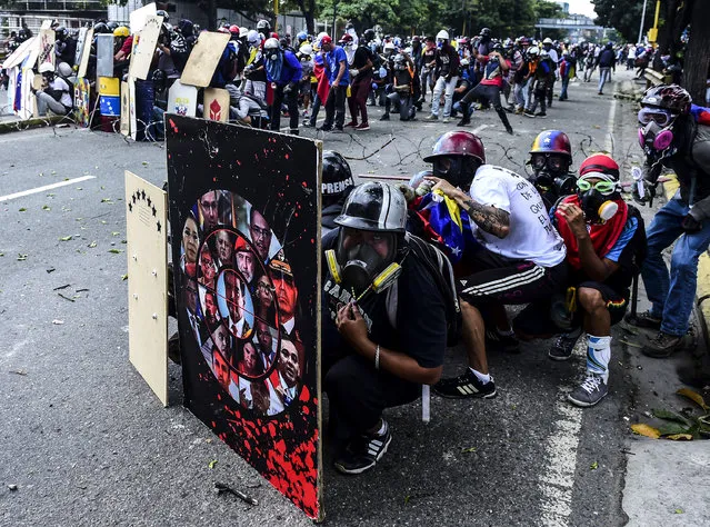 Opposition activists hide behind shields as they clash with the p[olice during a march towards the Supreme Court of Justice (TSJ) in an offensive against President Maduro and his call for Constituent Assembly in Caracas on July 22, 2017. The Legislative power, controlled by the opposition, appointed Friday a parallel supreme court in a public session claiming the TSJ judges had been illegally appointed by the parliament's former pro-government majority. (Photo by Ronaldo Schemidt/AFP Photo)