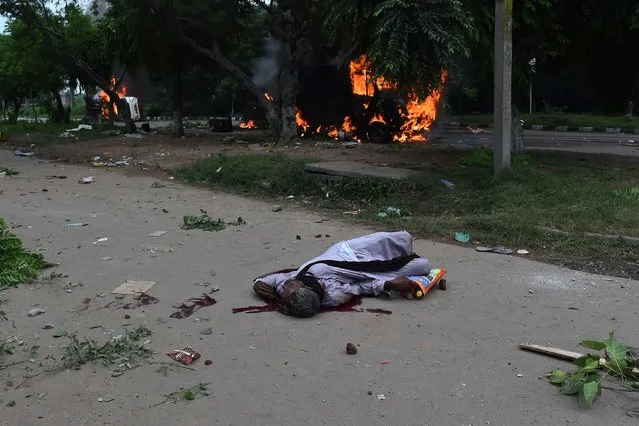 The dead body of a follower of Indian religious leader Gurmeet Ram Rahim Singh lays on the street next to burning vehicles following clashes between his supporters and security forces, after the controversial guru was convicted of rape, in Panchkula on August 25, 2017. At least four people were killed on August 25 when clashes broke out in northern India after a court convicted a controversial religious leader of raping two of his followers, sparking fury among tens of thousands of supporters who had gathered to await the verdict. (Photo by Money Sharma/AFP Photo)