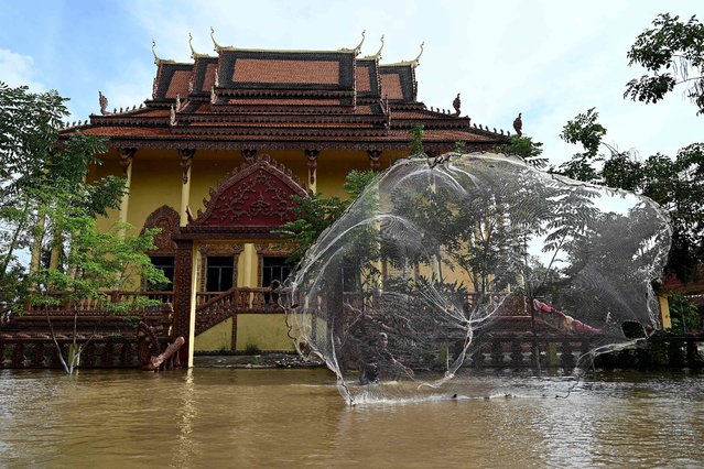 A man throws a fishing net into floodwaters at a temple on the outskirts of Phnom Penh, Cambodia on October 21, 2023. (Photo by Tang Chhin Sothy/AFP Photo)