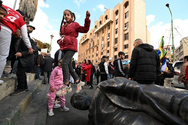 A girl jumps off a toppled statue of former president Hafez al-Assad as people gather on a street in Sweida on December 13, 2024, to celebrate the collapse of his son Bashar al-Assad's rule. Islamist-led rebels took Damascus in a lightning offensive on December 8, ousting president Bashar al-Assad and ending five decades of Baath rule in Syria. (Photo by Louai Beshara/AFP Photo)