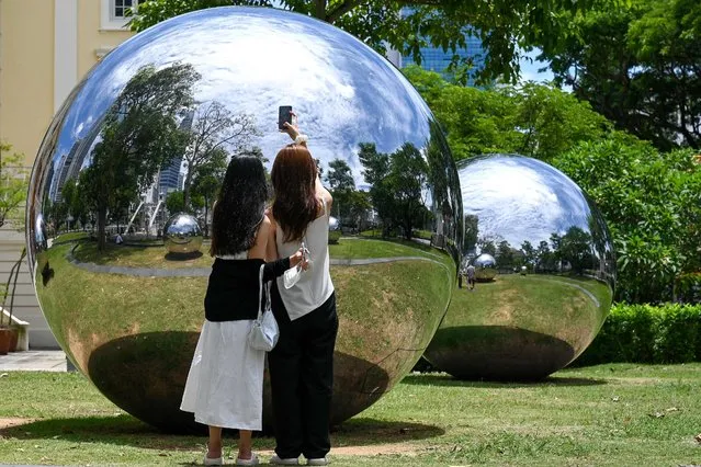 Women pose for photographs infront of an art installation comprising of reflective stainless steel balls at a public park in Singapore on August 22, 2022. (Photo by Roslan Rahman/AFP Photo)