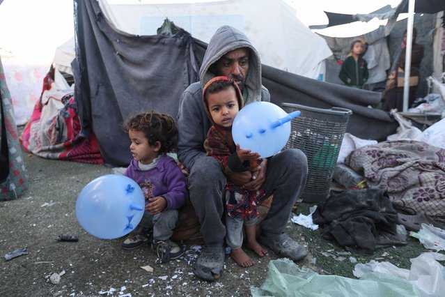 A man sits with two children, as Palestinians inspect the damage at a tent camp sheltering displaced people, following an Israeli strike, amid the Israel-Hamas conflict, in Deir Al-Balah in the central Gaza Strip, on December 15, 2024. (Photo by Ramadan Abed/Reuters)