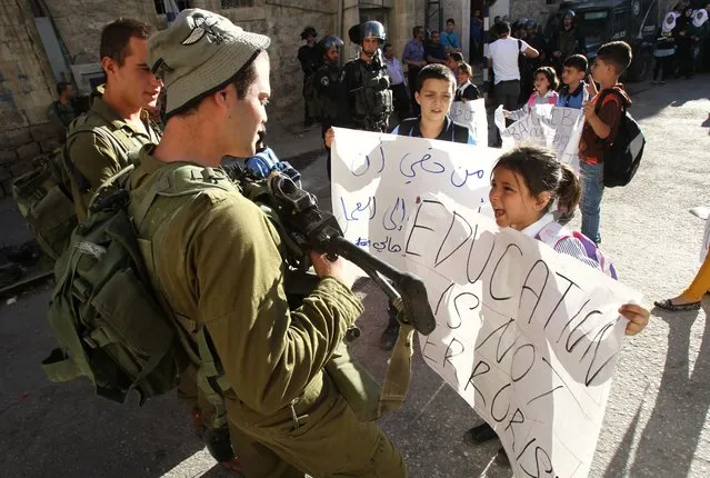 Palestinian children demonstrate near an Israeli check point in the centre of the West Bank city of Hebron after they couldn't pass the checkpoint to get to school as it was closed off by Israeli security forces on August 26, 2014. (Photo by Hazem Bader/AFP Photo)